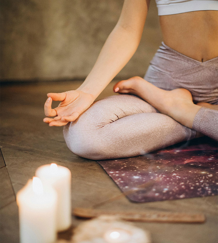 A person seated cross-legged in a meditation pose beside lit candles